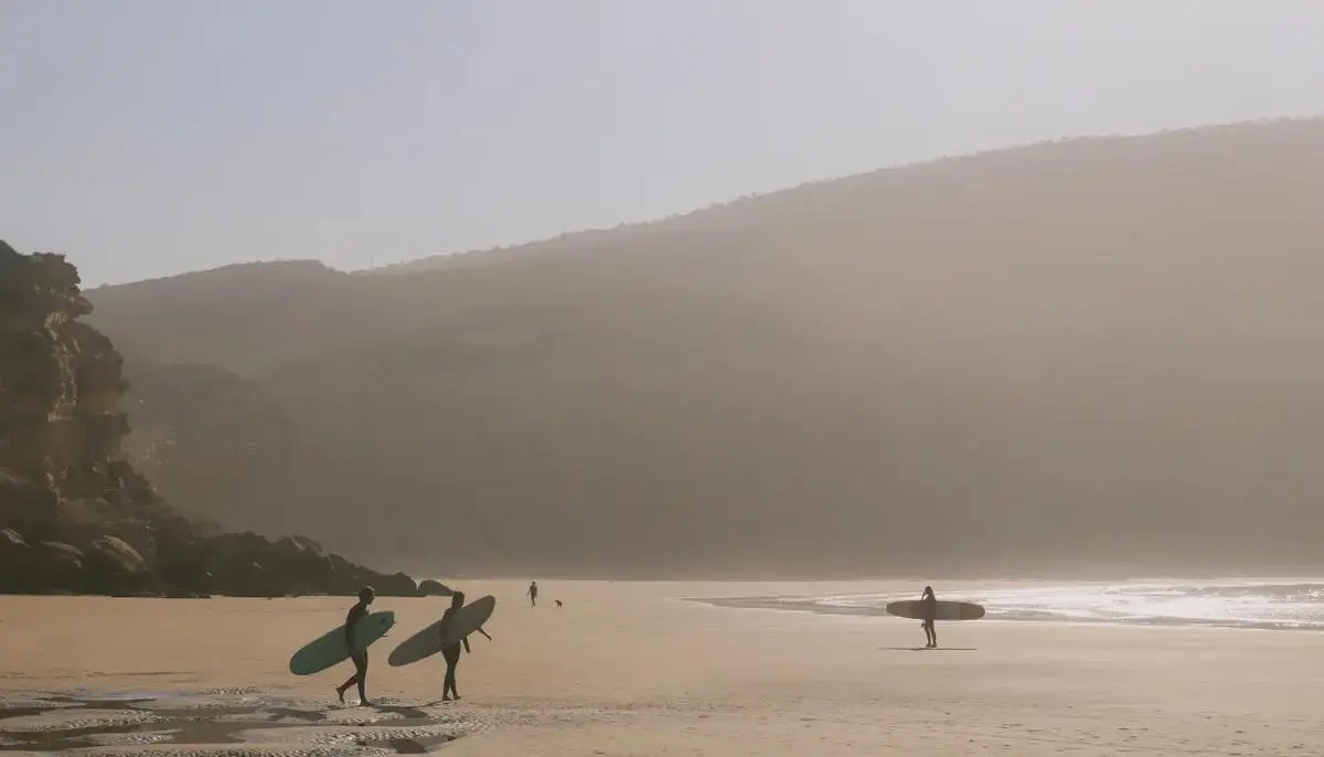 Surf tours Morocco — surfers carrying boards along misty Atlantic beach morning