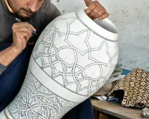 Moroccan handicrafts — artisan hand-drawing geometric patterns on large pottery vase in Fes workshop