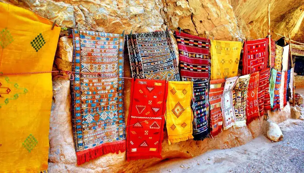 Moroccan rugs display on rock wall souk — traditional Berber carpets hanging for sale in Morocco